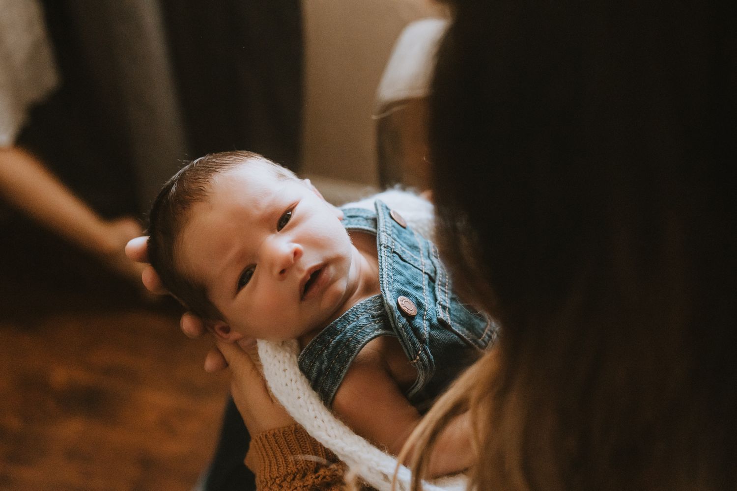 Newborn baby in blue outfit looks up during indoor portrait session.