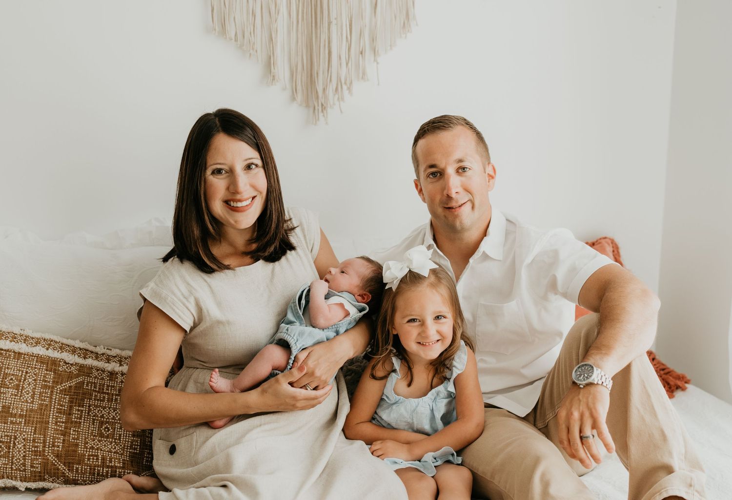 Happy family with young children posing together on couch against white wall with macrame decor.