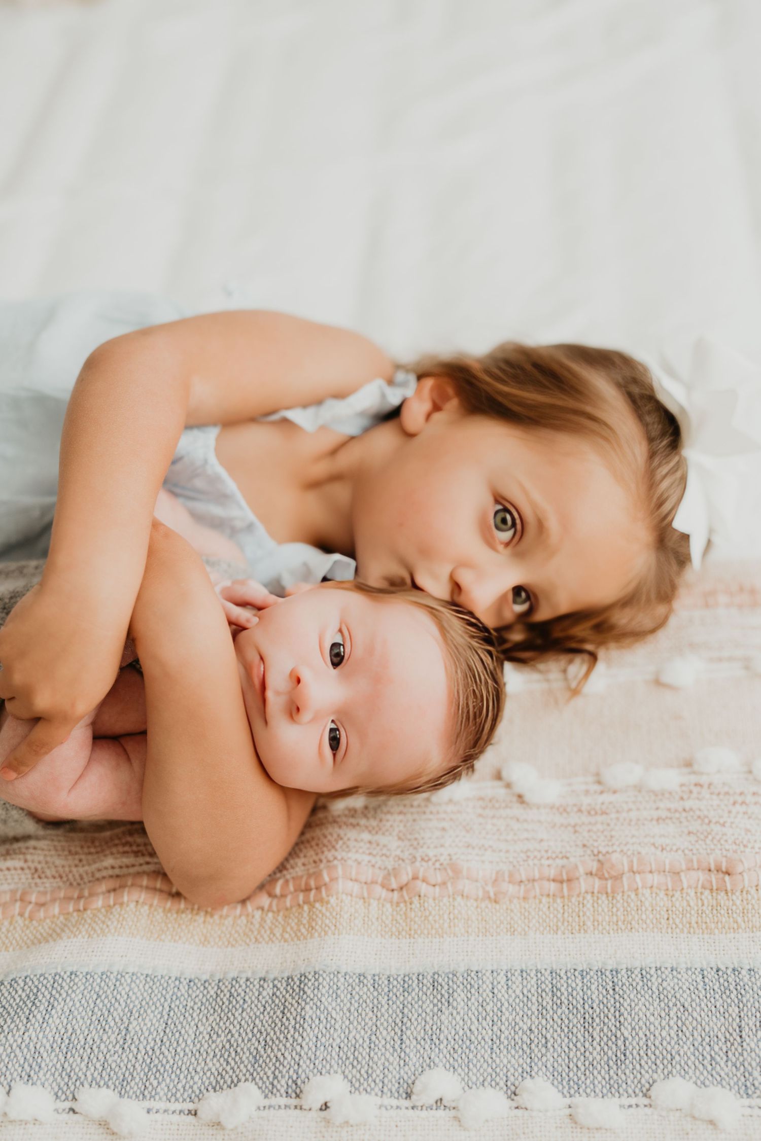 Two siblings sharing tender moment while laying on textured blanket.
