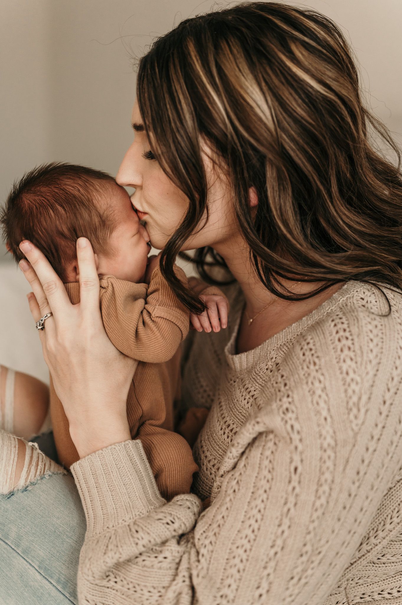 Intimate portrait of parent giving gentle kiss to newborn baby in knit sweater.