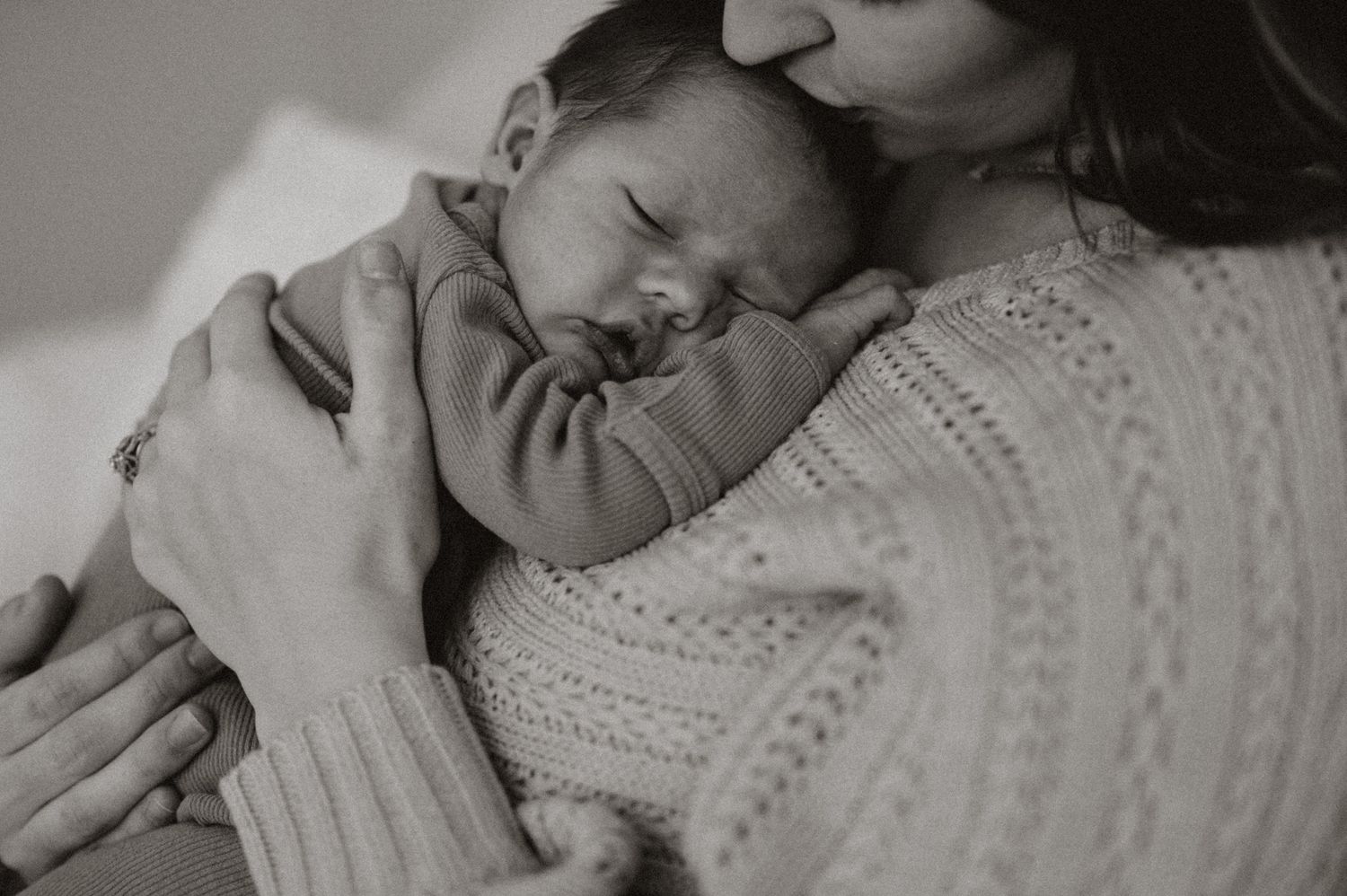 A peaceful black and white image of a sleeping newborn baby cradled in soft knitted clothing.