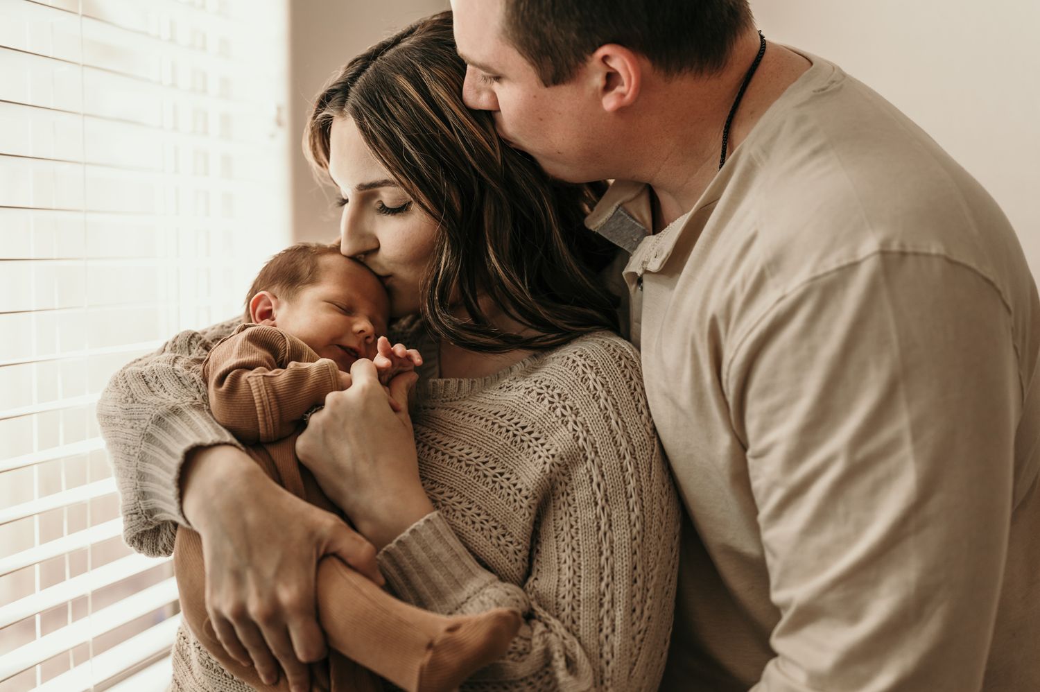 Tender family moment with newborn baby by window in natural light.