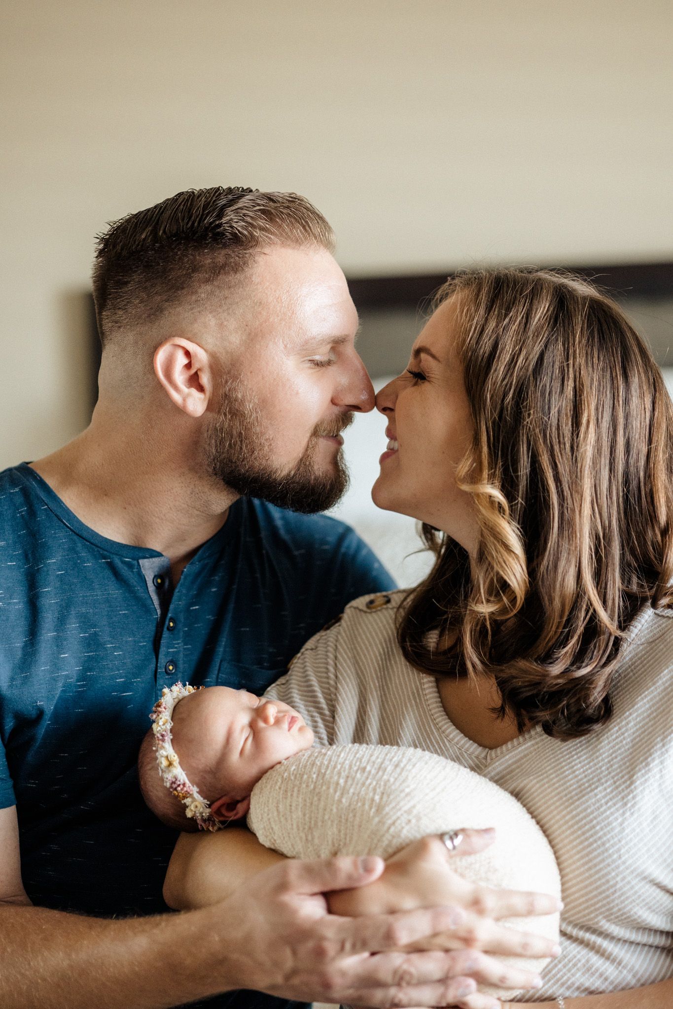 An intimate family portrait capturing parents sharing a loving moment while cradling their sleeping newborn.