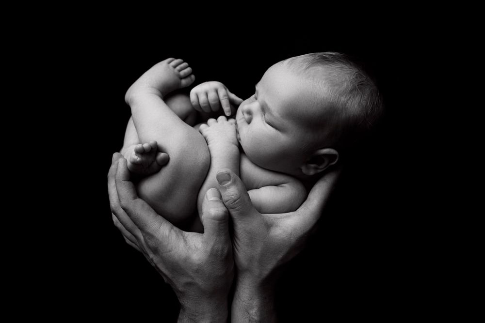 A newborn baby cradled in adult hands against a dark background.