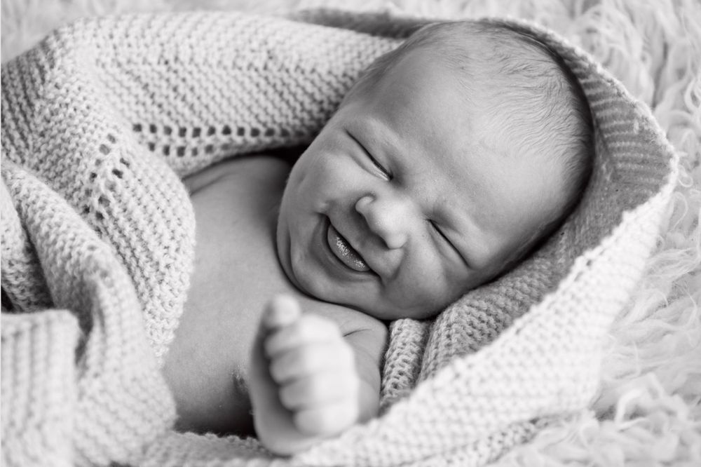 A newborn baby smiles while wrapped in a soft knitted blanket in black and white.