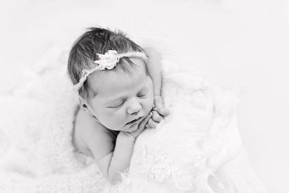 Newborn baby sleeping on white lace with delicate headband in black and white.