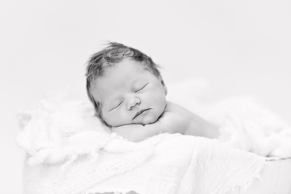 Sleeping newborn peacefully resting on soft white bedding in monochrome.