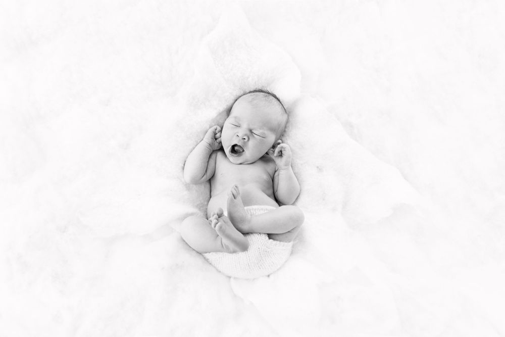 A sleeping newborn curled up on white textured fabric in high key photography.