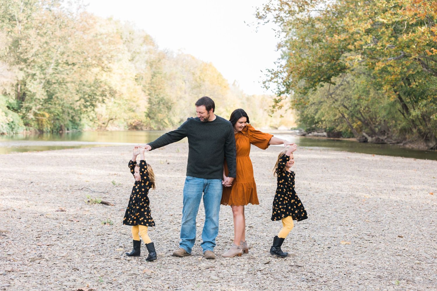 A playful family portrait on a riverbank during autumn with matching outfits.