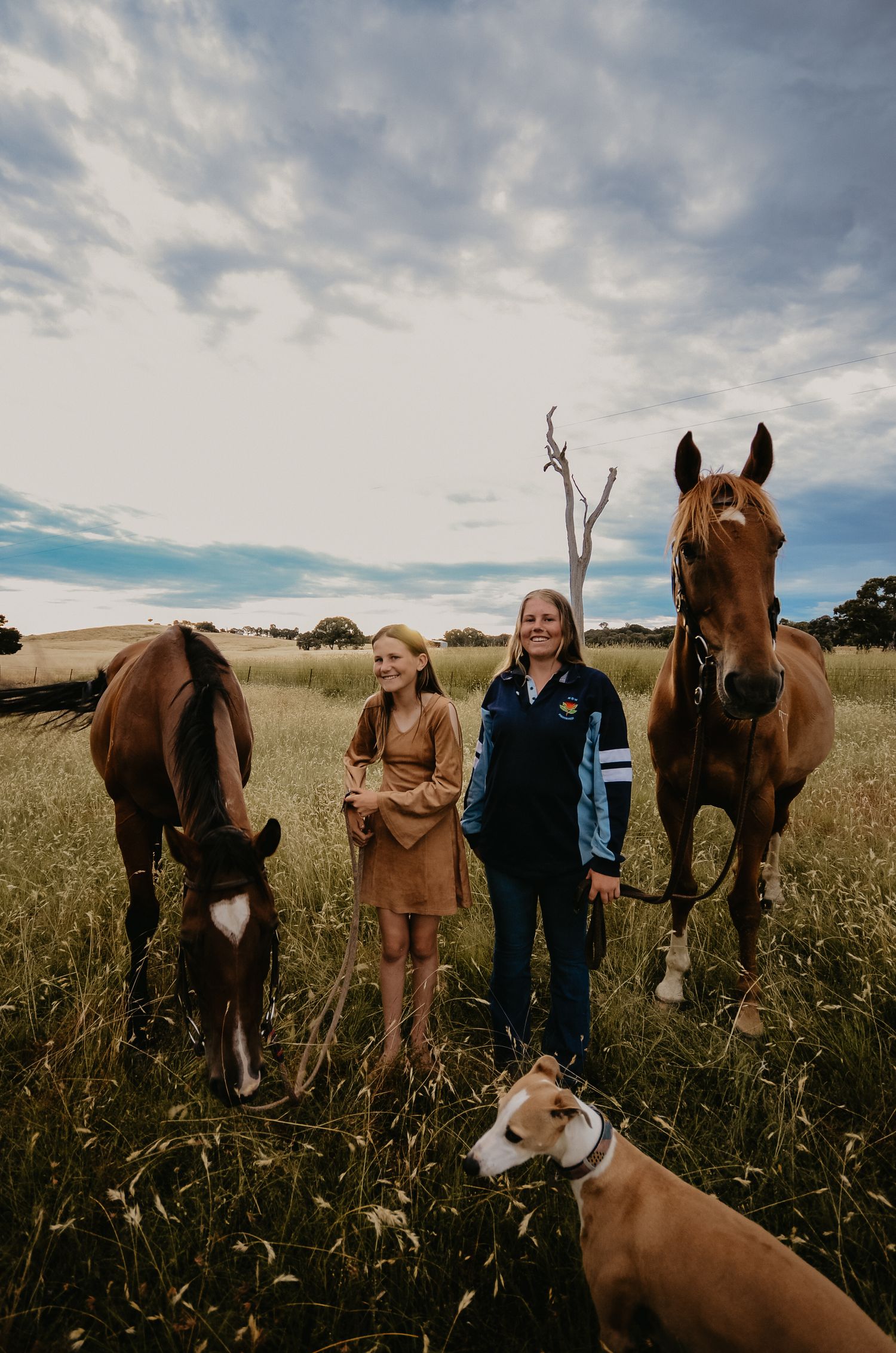 two girls standing in a long grass paddock next to their horses and a dog at Gundaroo NSW