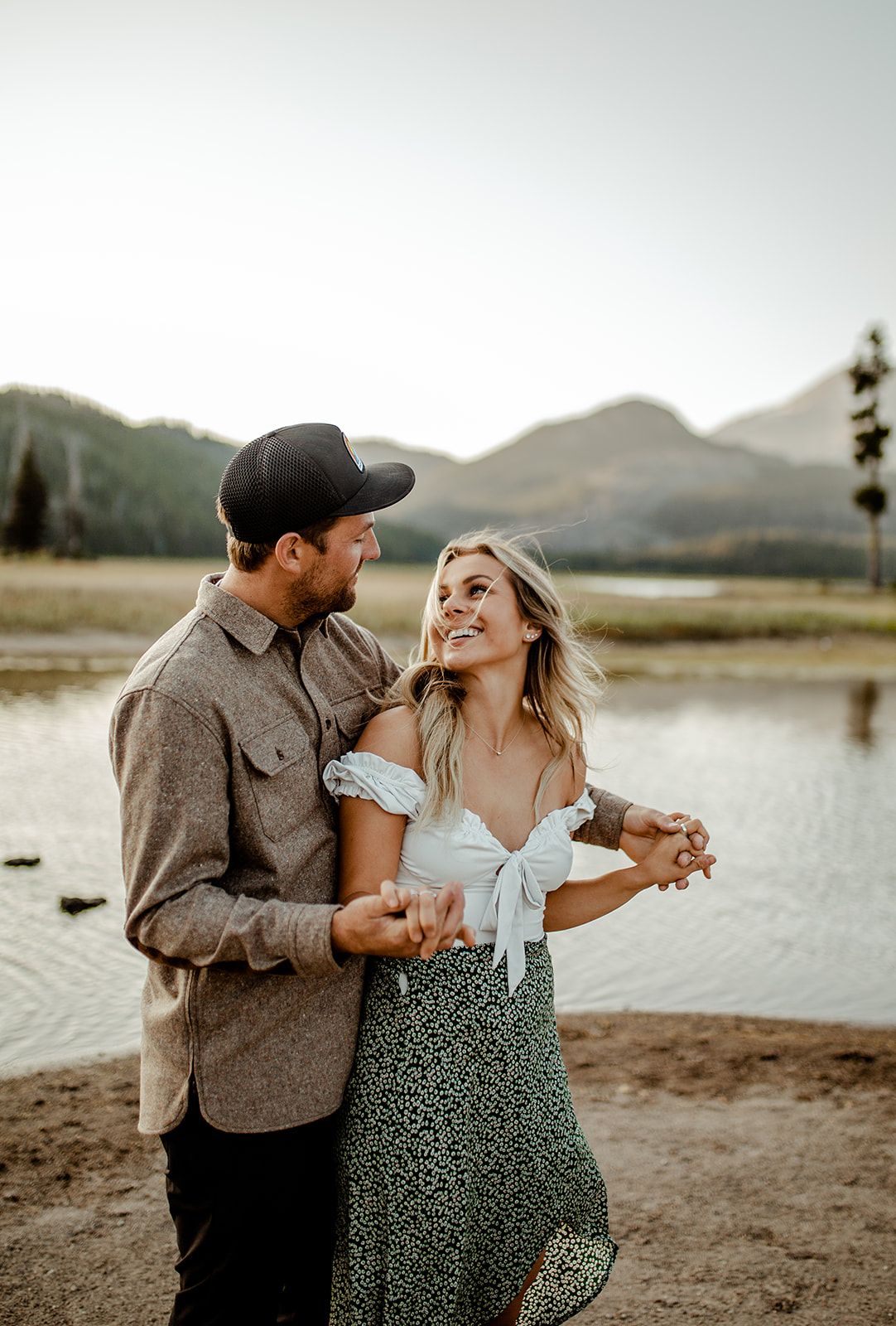 Dancing couple sharing romantic moment by mountain lake at sunset.
