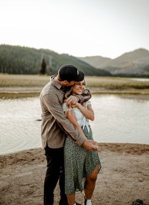 Intimate moment between couple by mountain lake during sunset.