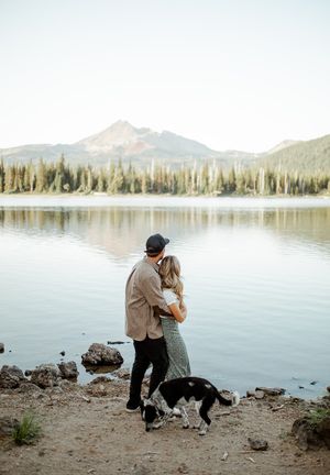 Couple sharing a tender moment by a serene mountain lake with their dog.