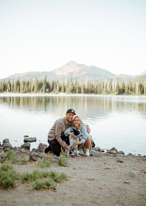 Person and dog share tender moment by serene mountain lake at sunset.