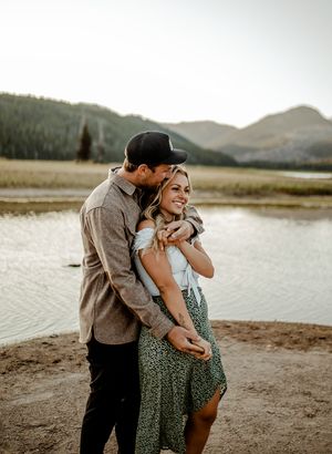 Loving embrace on lakeshore with mountain backdrop at golden hour.