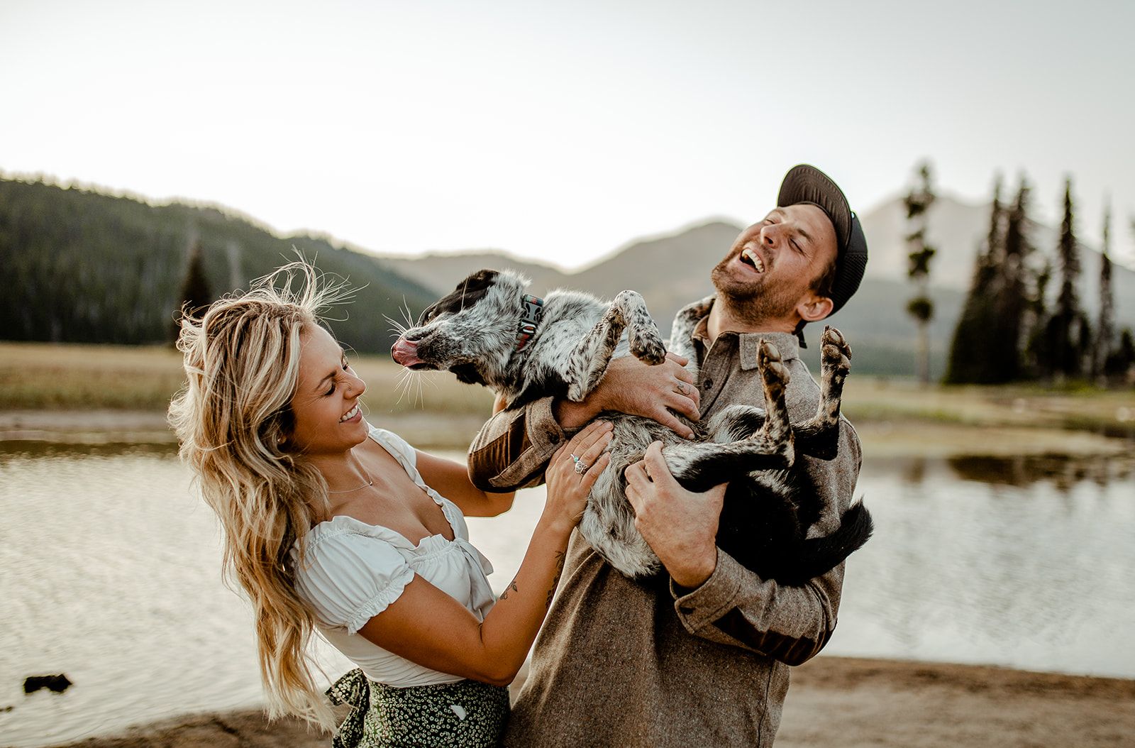 Joyful couple playing with their dogs by mountain lake.
