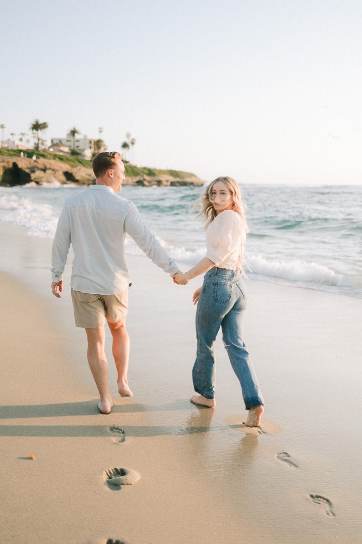 Couple walking hand in hand on a scenic beach with palm trees and ocean waves in the background.