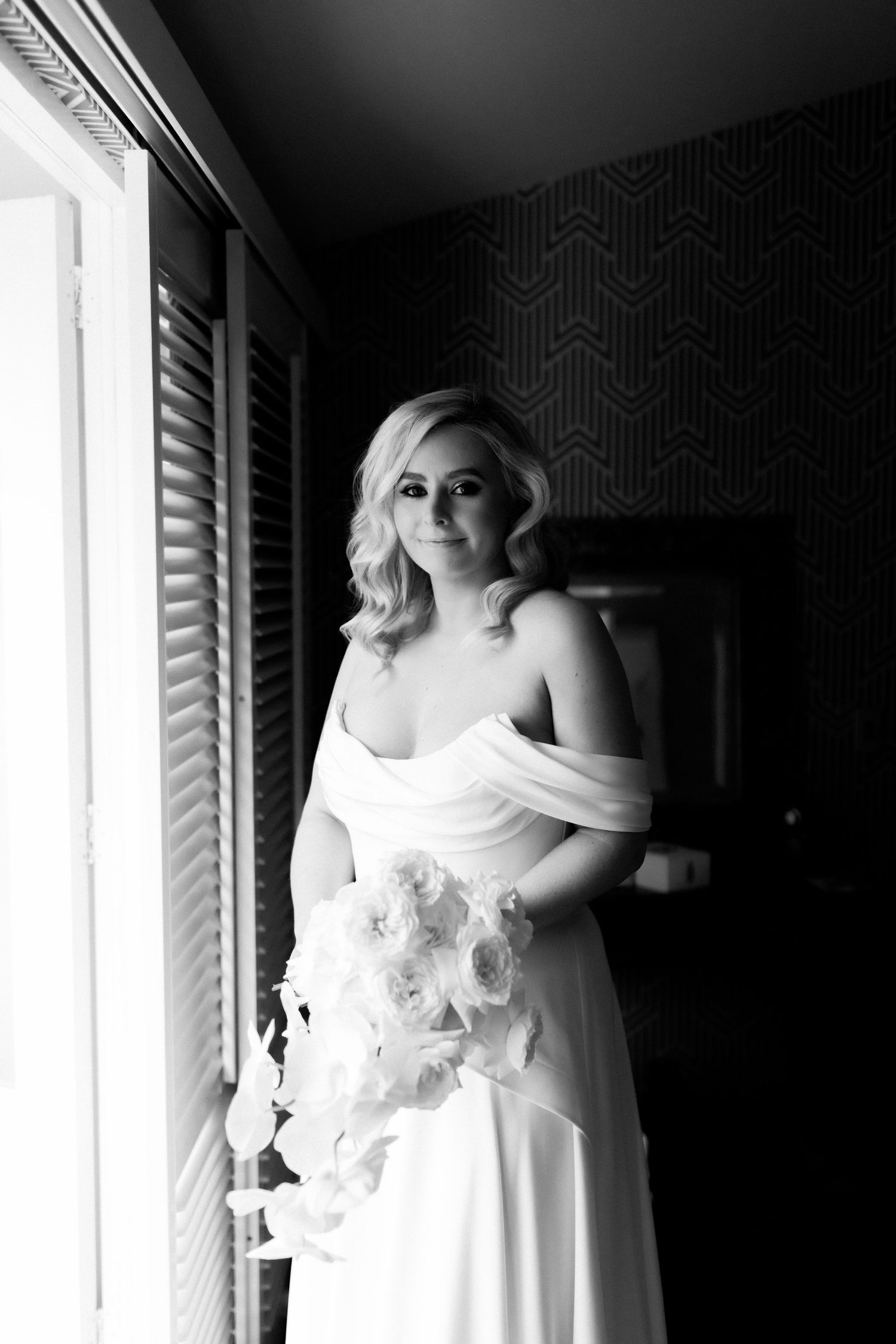 Artistic black and white bridal portrait by window with geometric wallpaper.