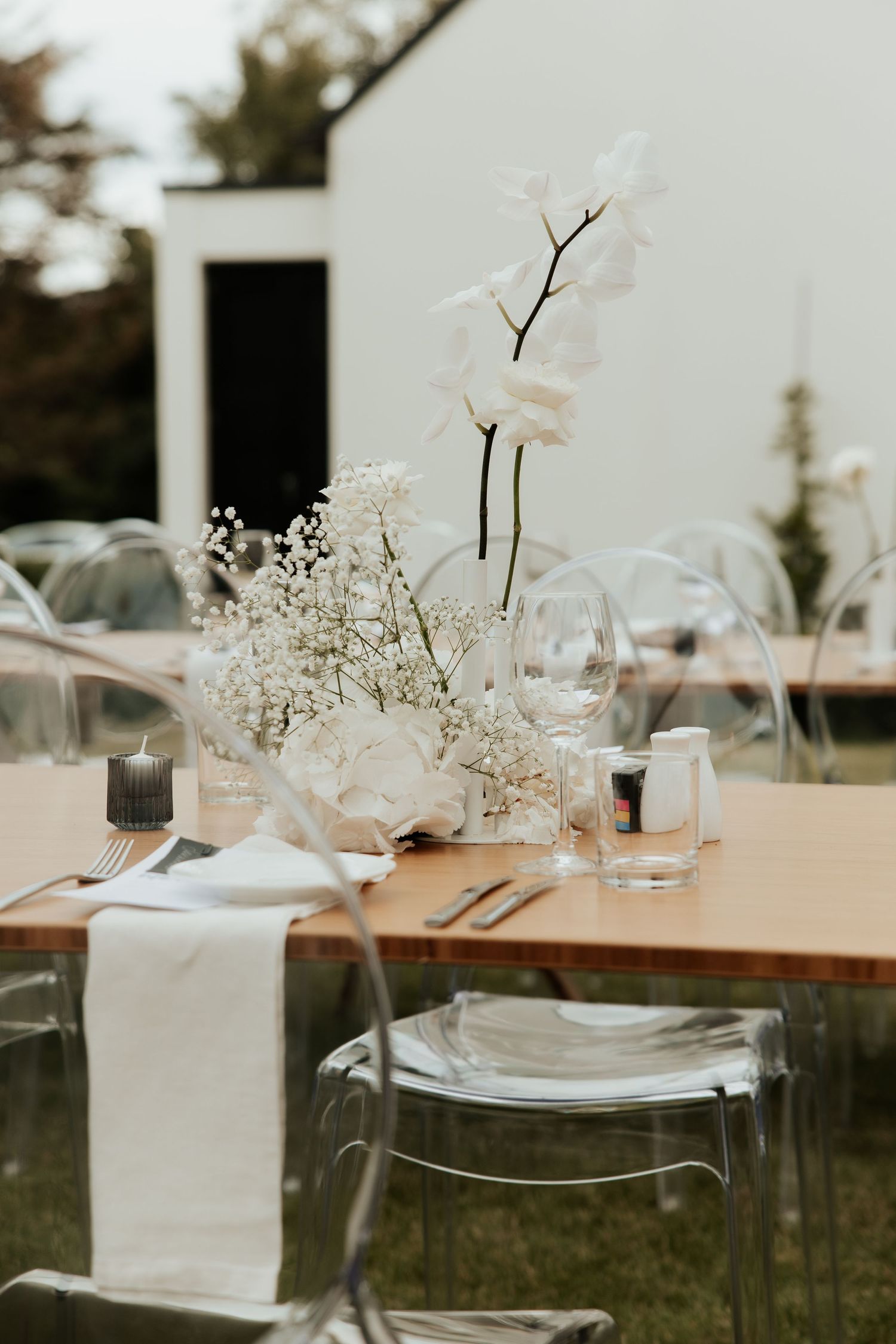 Elegant wedding table setting with white orchid centerpiece and clear ghost chairs.