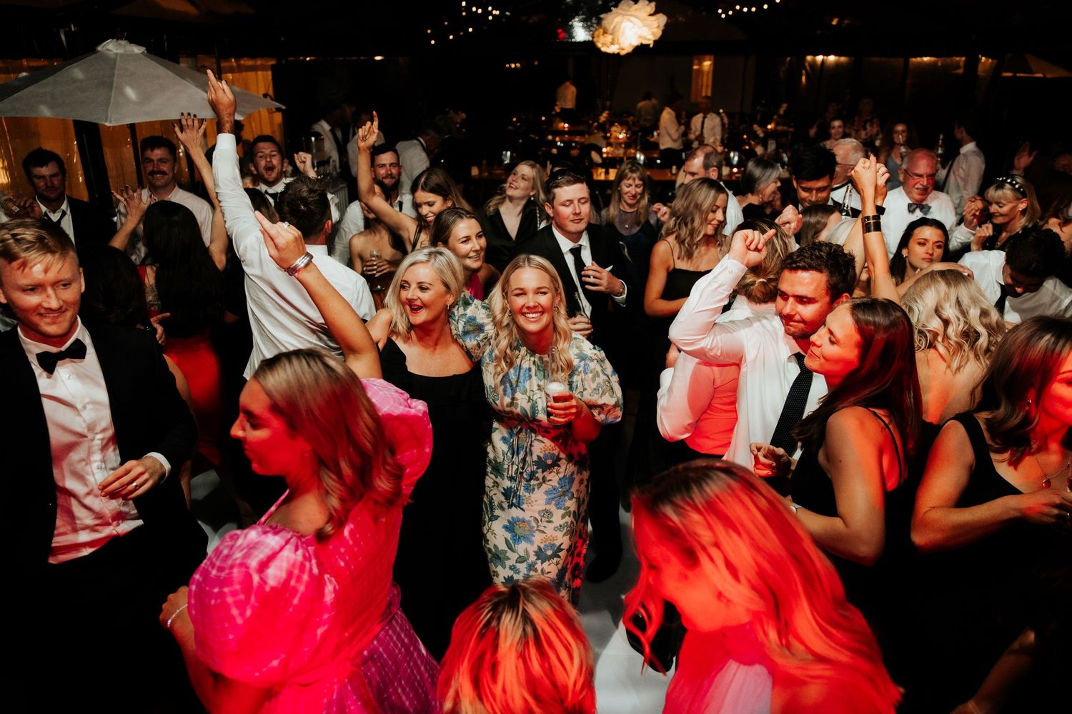 Energetic wedding reception with crowd of guests dancing under colorful lights.