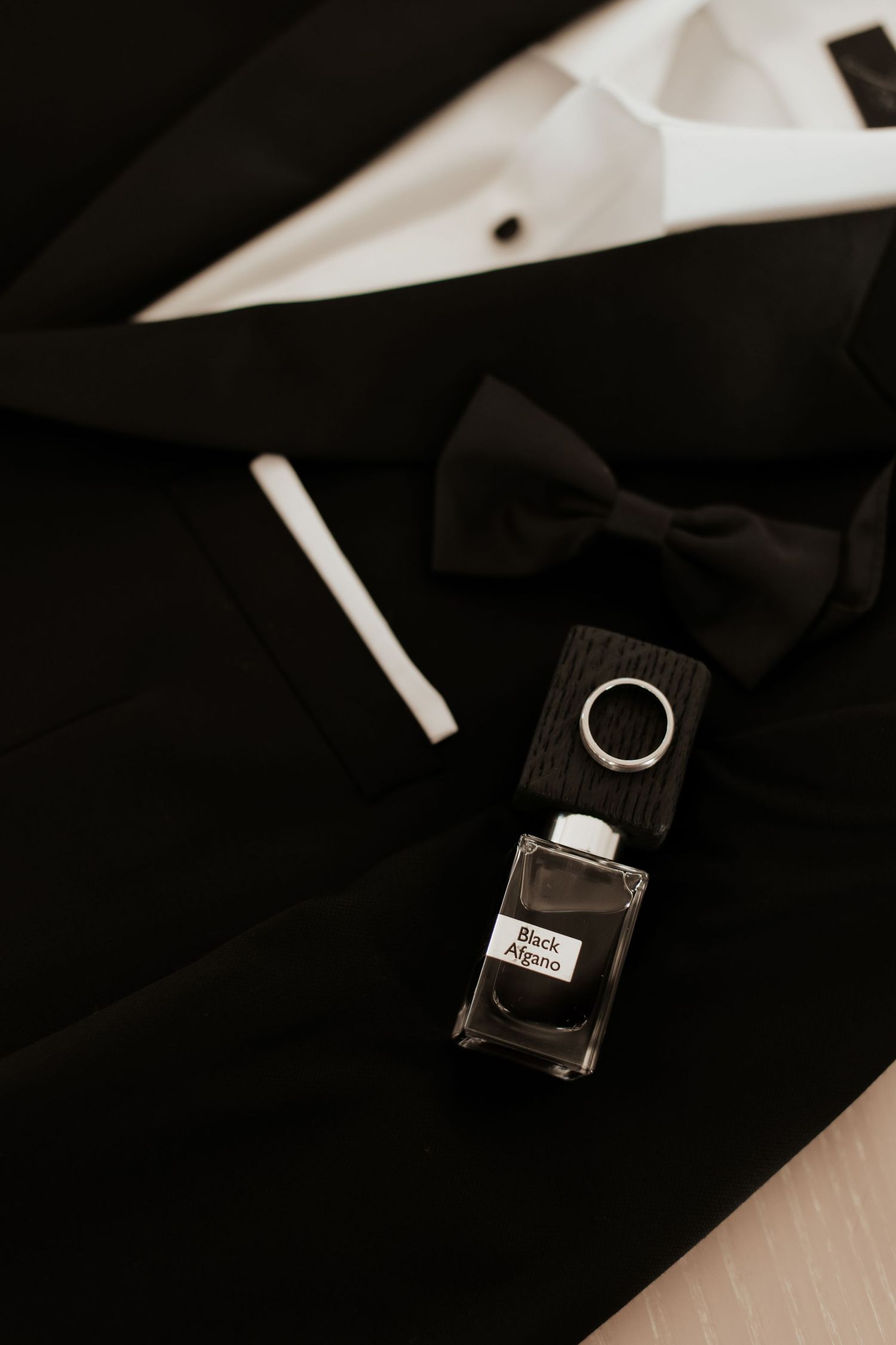 Black bowtie and cologne bottle arranged on dark fabric.