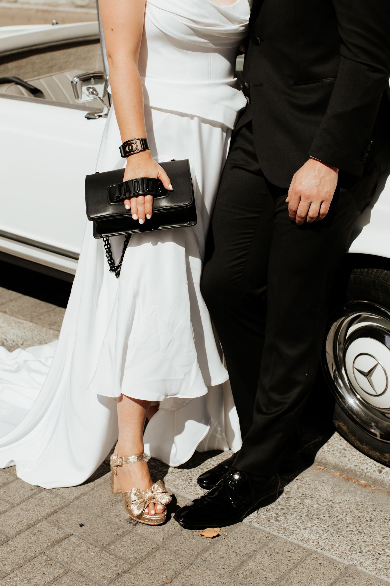 Detail shot of formal attire and black handbag next to vintage Mercedes-Benz wheel.