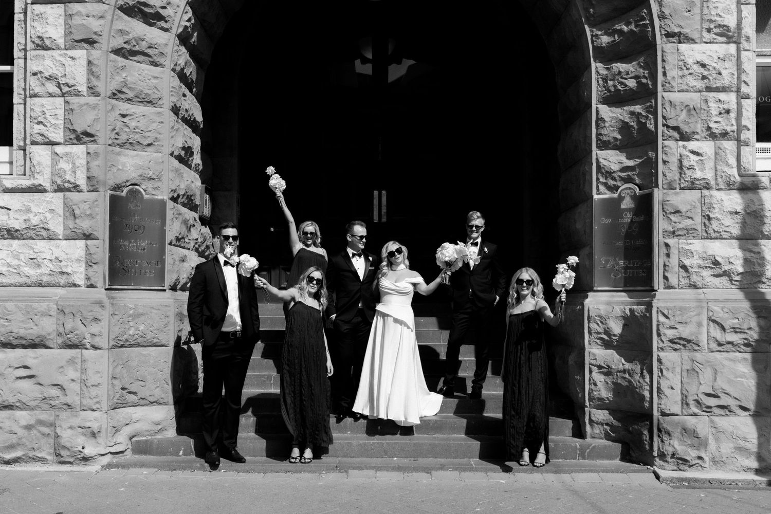 Wedding party celebrates with joy under a stone archway entrance.