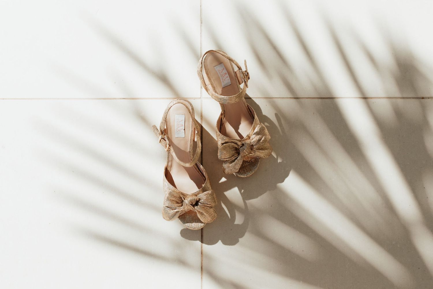 Elegant beige wedding heels casting palm leaf shadows on white surface.
