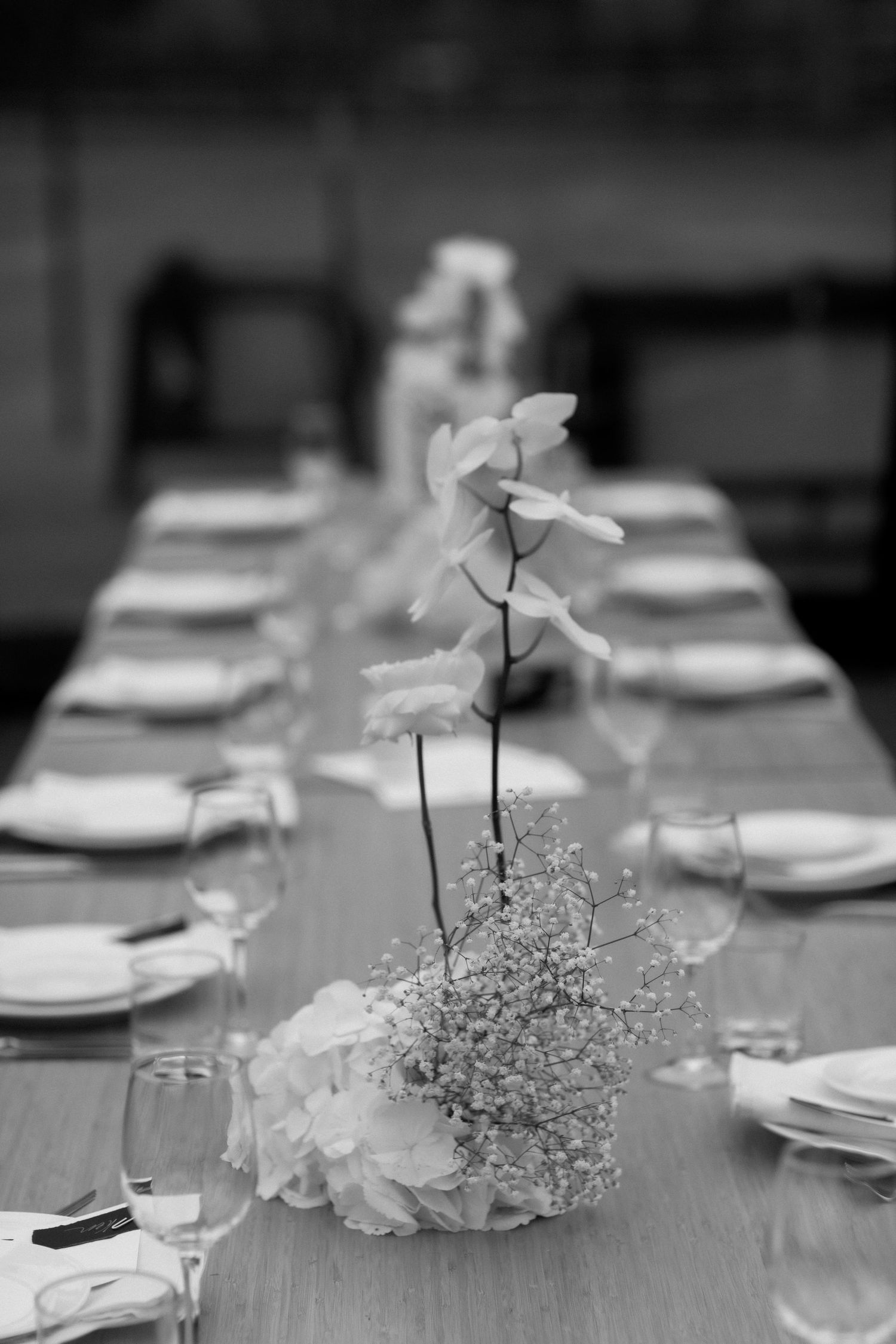 Black and white photo of an elegant table setting with delicate white floral centerpieces.