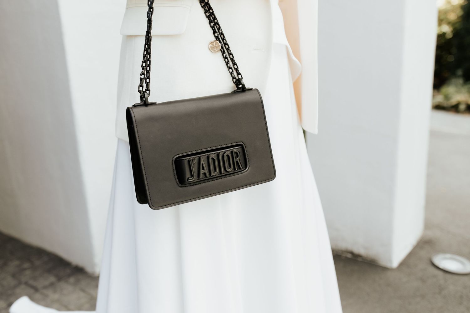 Close-up of a black leather handbag with chain strap against a white dress background.