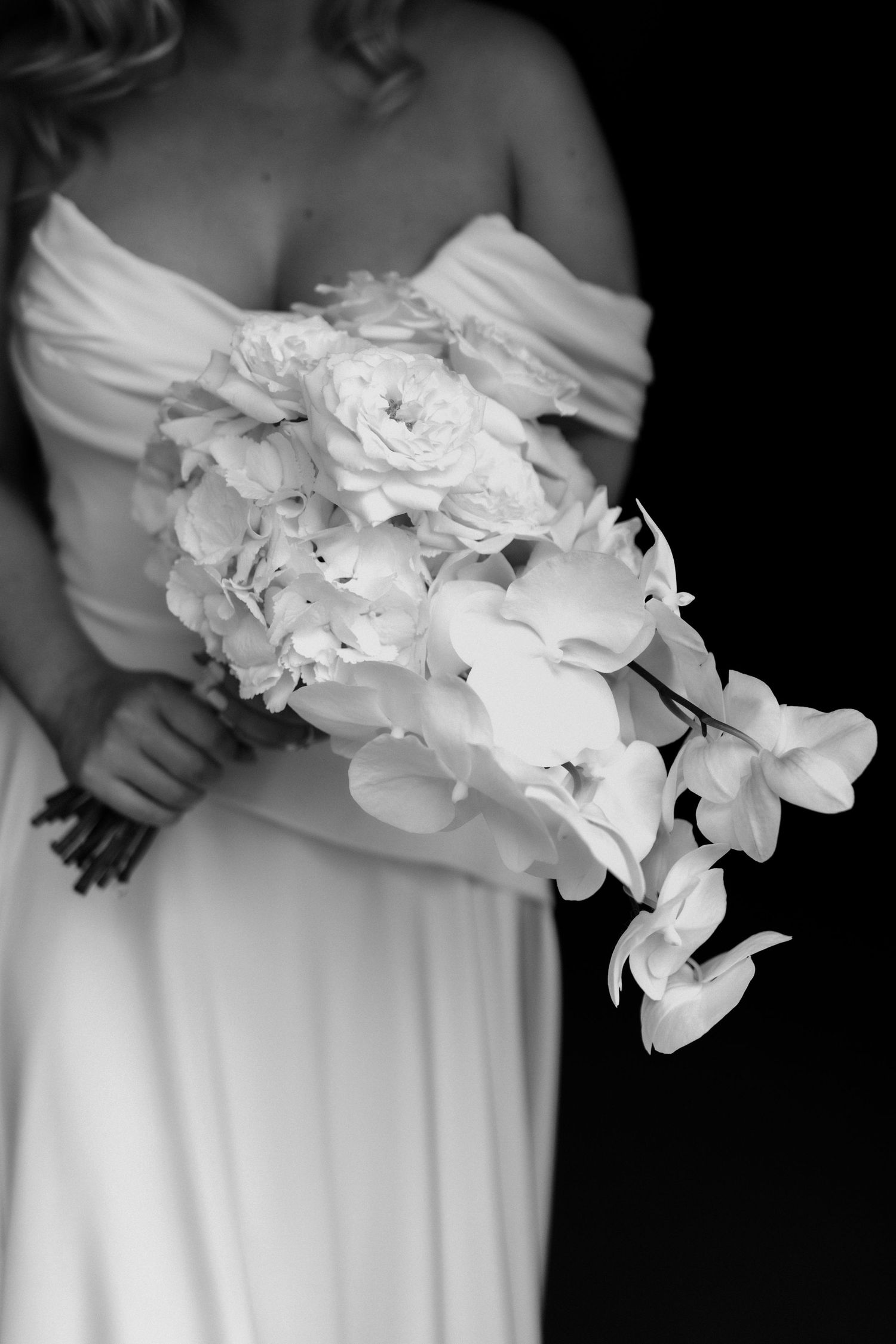 Close-up of white orchid and rose bridal bouquet against black background.