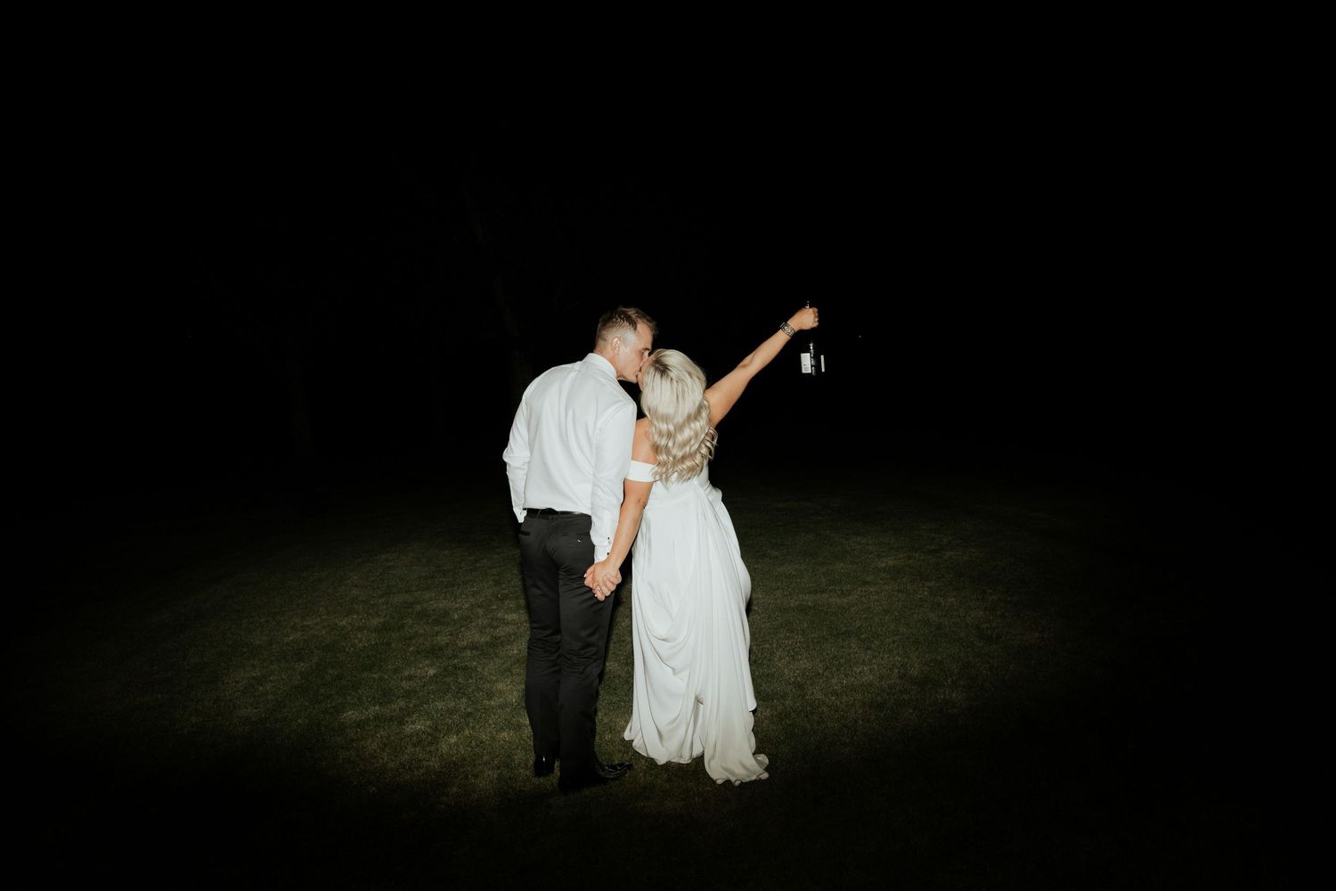 A couple dancing under a spotlight on a dark outdoor dance floor.