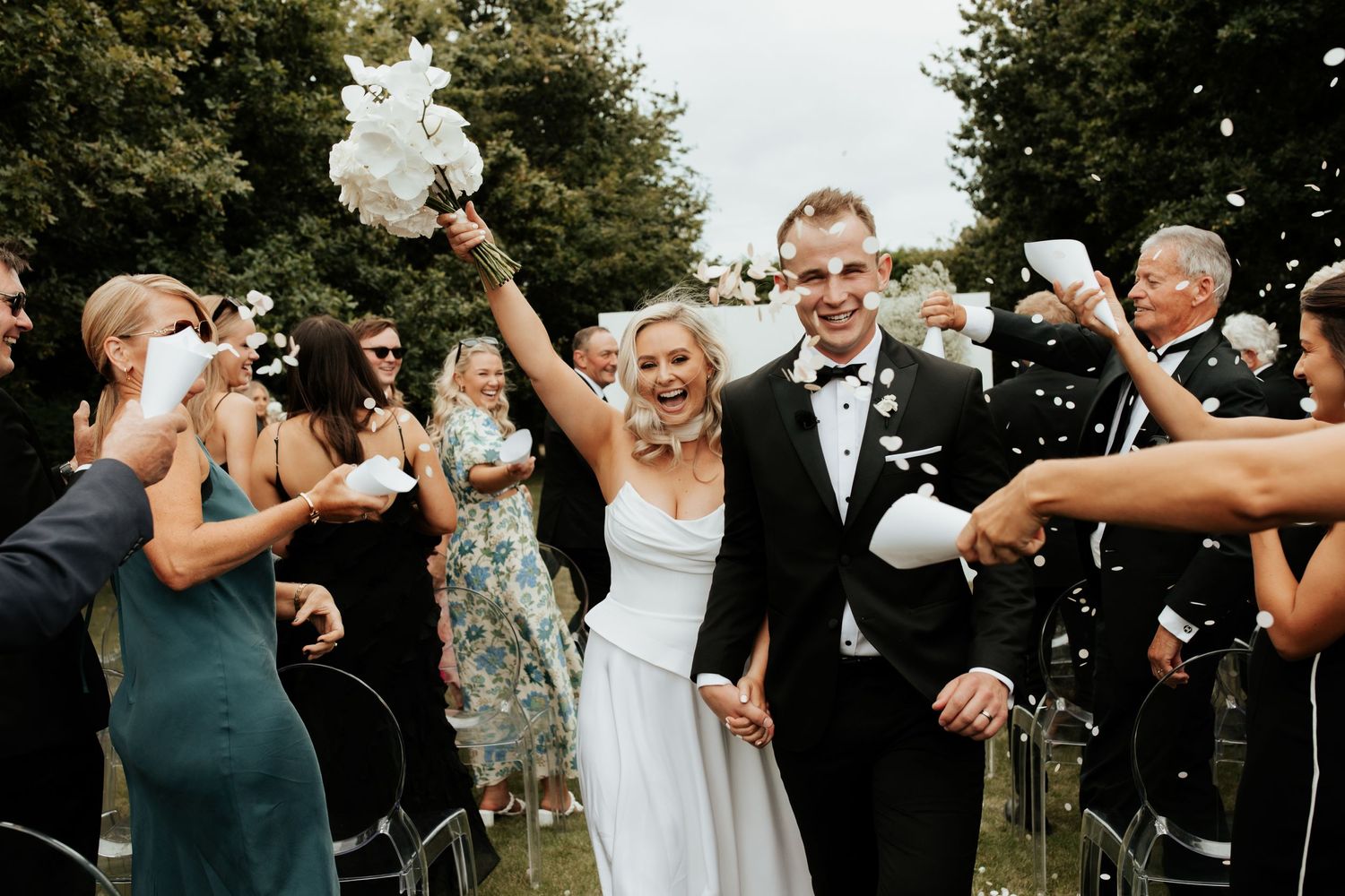 Joyful wedding celebration with guests throwing confetti as couple exits ceremony.