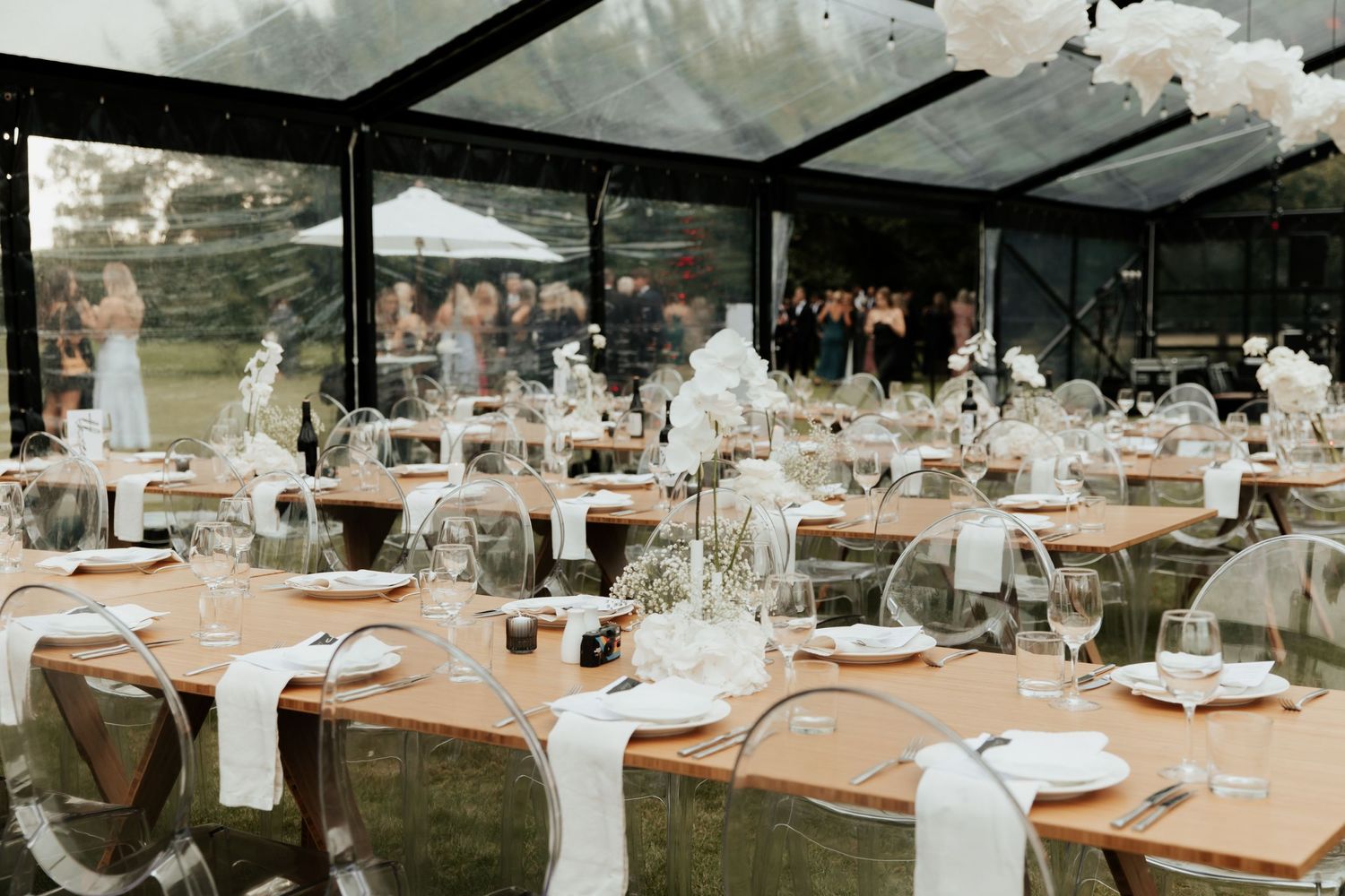 Covered outdoor wedding reception with tables set under a clear tent canopy.