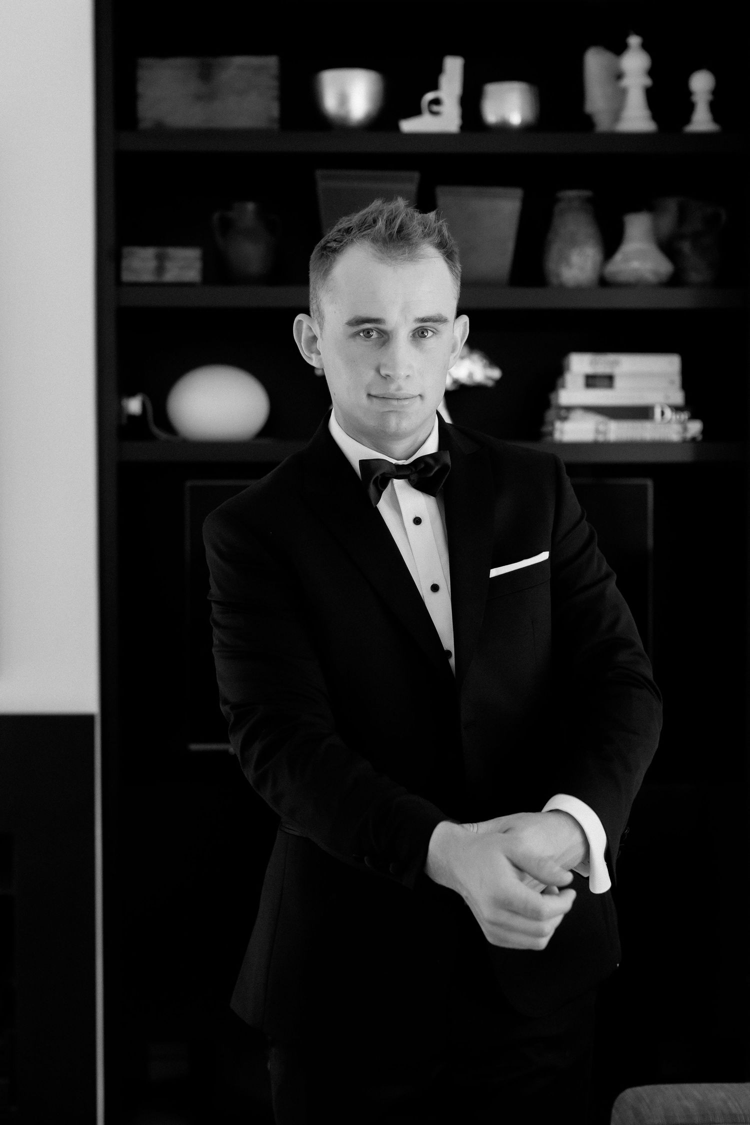 Formal black tuxedo with bow tie photographed against dark bookshelf background.