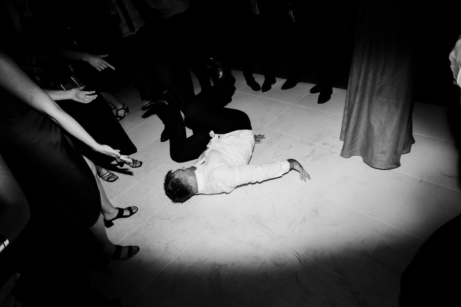A dramatic black and white shot of someone lying on a dance floor surrounded by people.