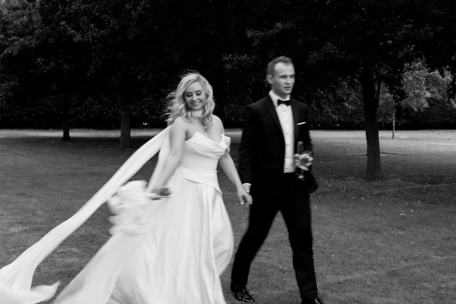 Black and white photo of couple walking through garden in wedding attire.