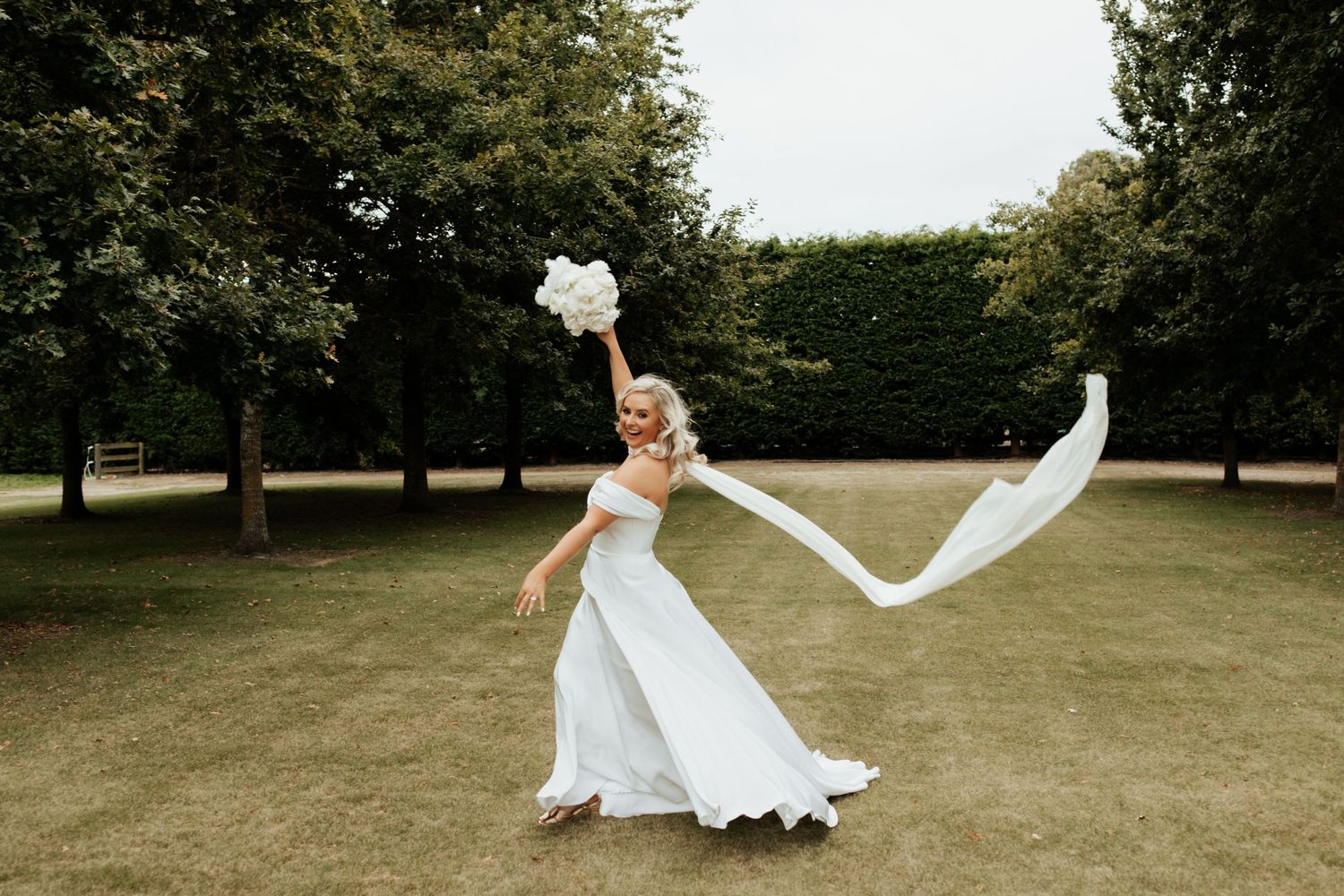Bride twirling in flowing white dress with veil floating in breeze.