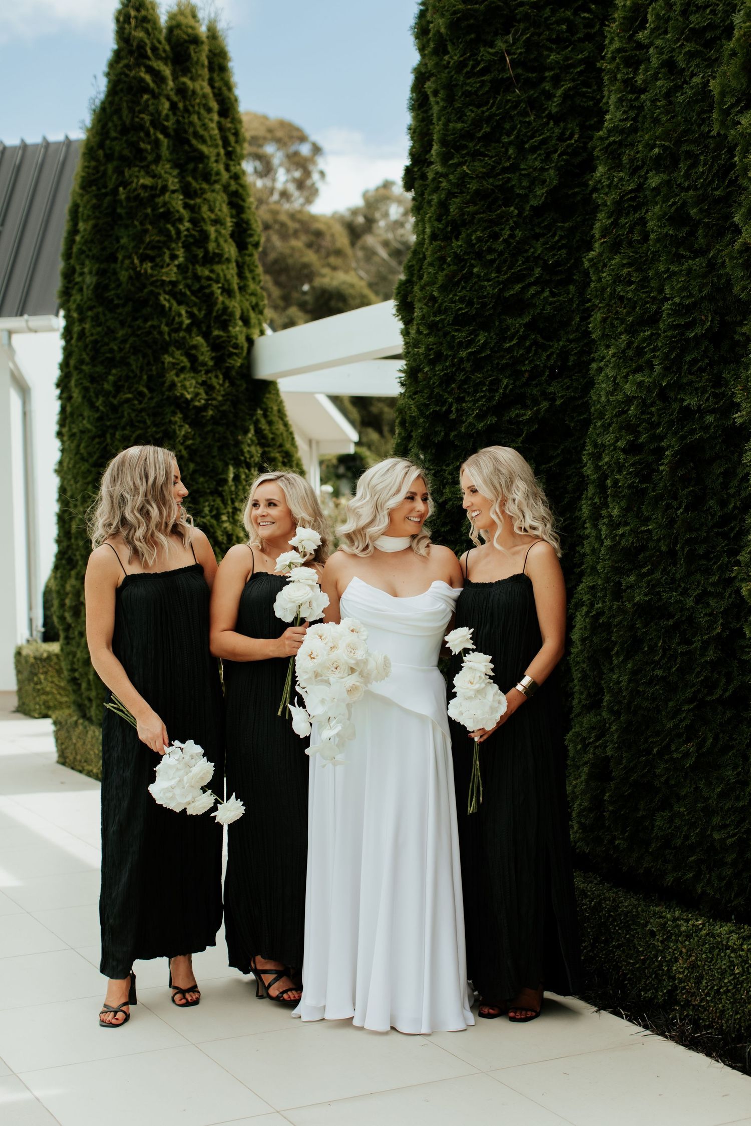 Wedding party in black and white dresses holding orchids pose against modern architecture.