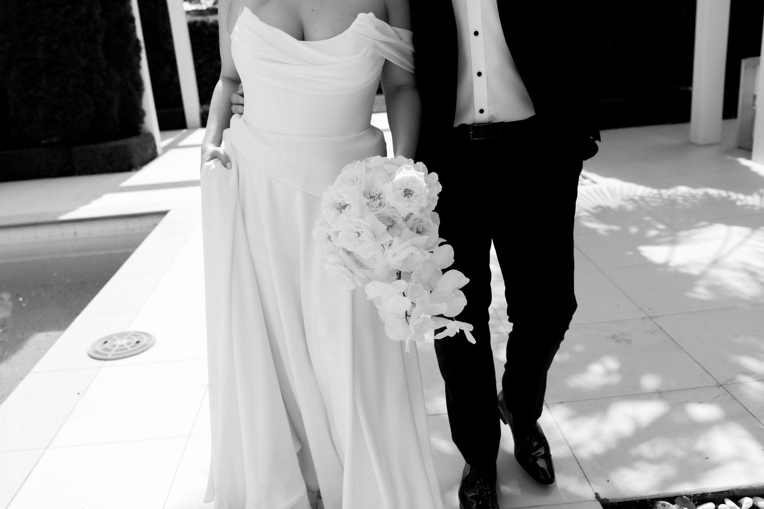 Black and white photo capturing flowing wedding dress detail under pergola.