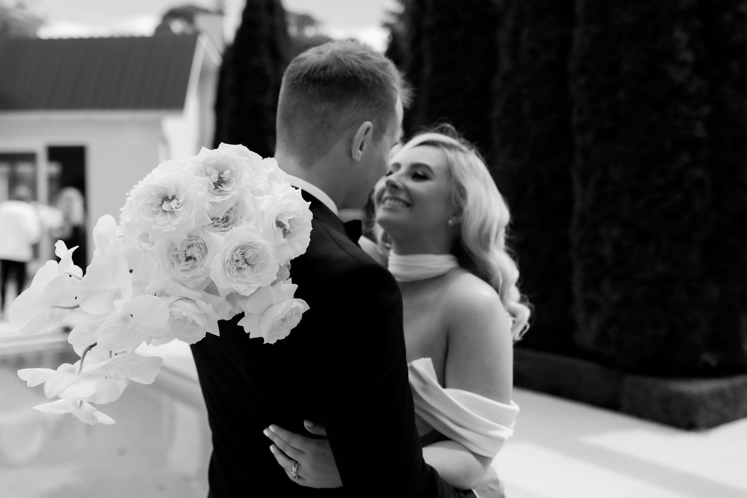 Black and white photo of couple embracing with white floral bouquet.