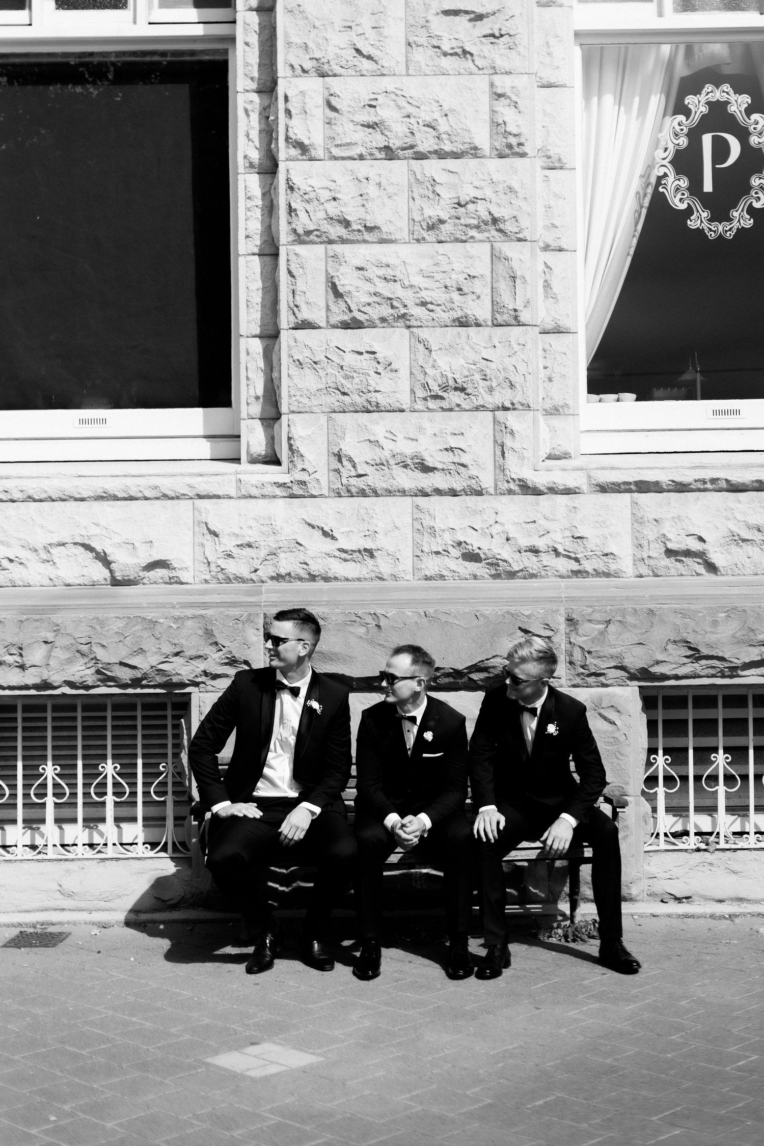 Three men in formal suits sitting on a bench outside a stone building.