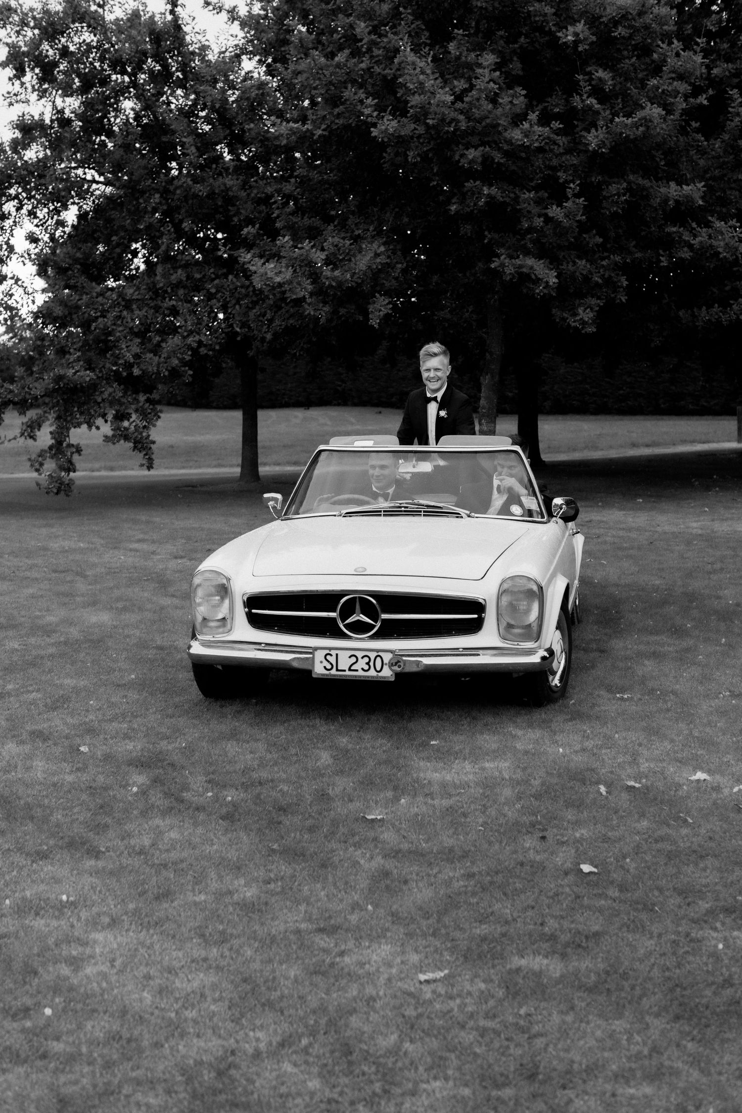 Vintage Mercedes-Benz convertible on grass with someone in formal attire.