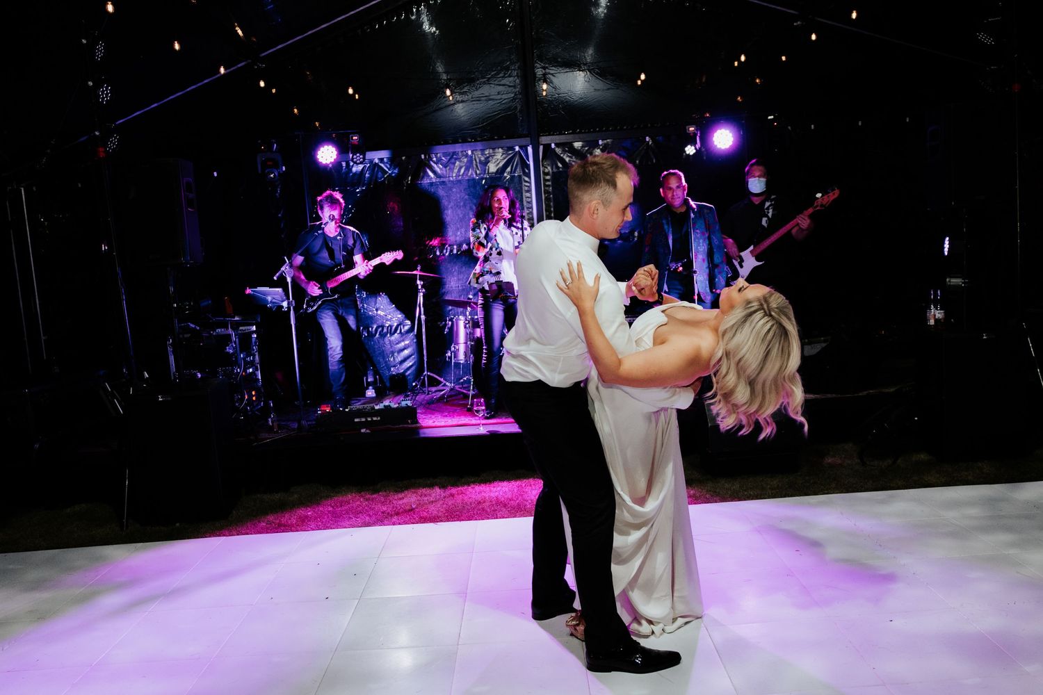 First dance at wedding reception with live band performing on stage in purple lighting.