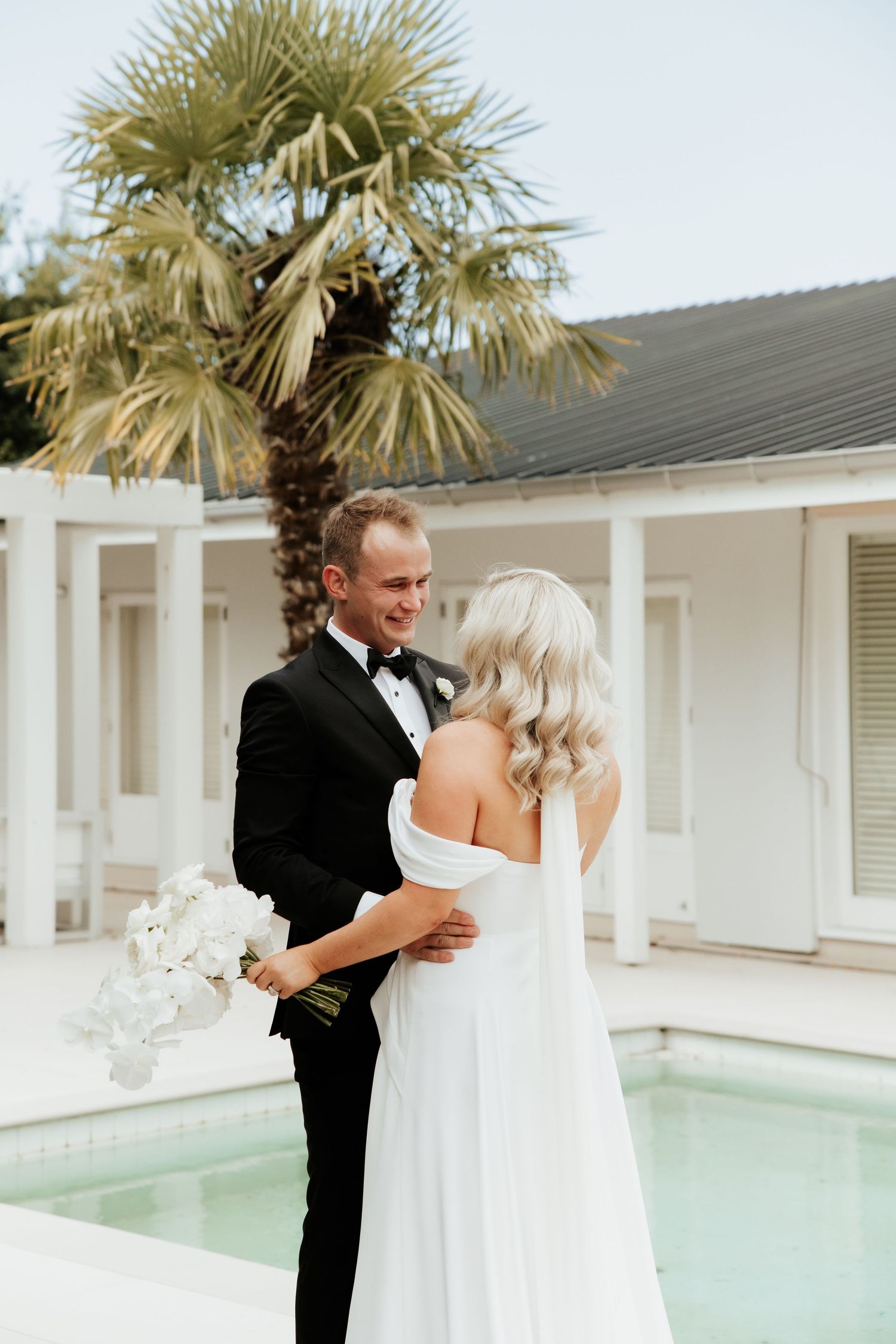 Romantic first look moment between couple by pool with palm trees.