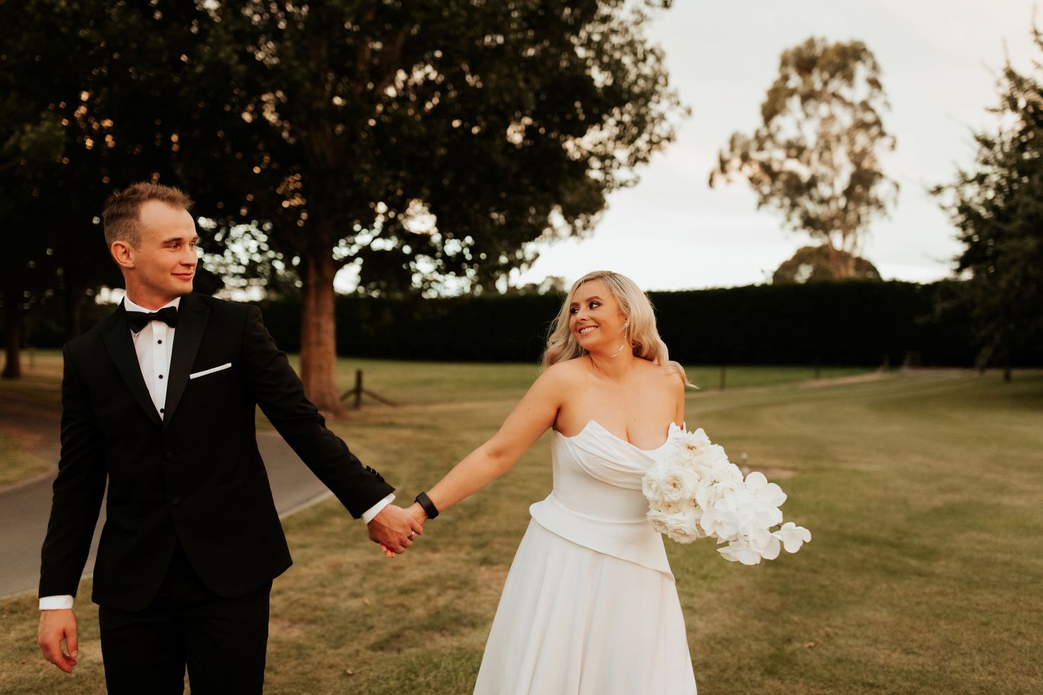 Happy couple walking hand in hand on a grassy lawn during their wedding day.