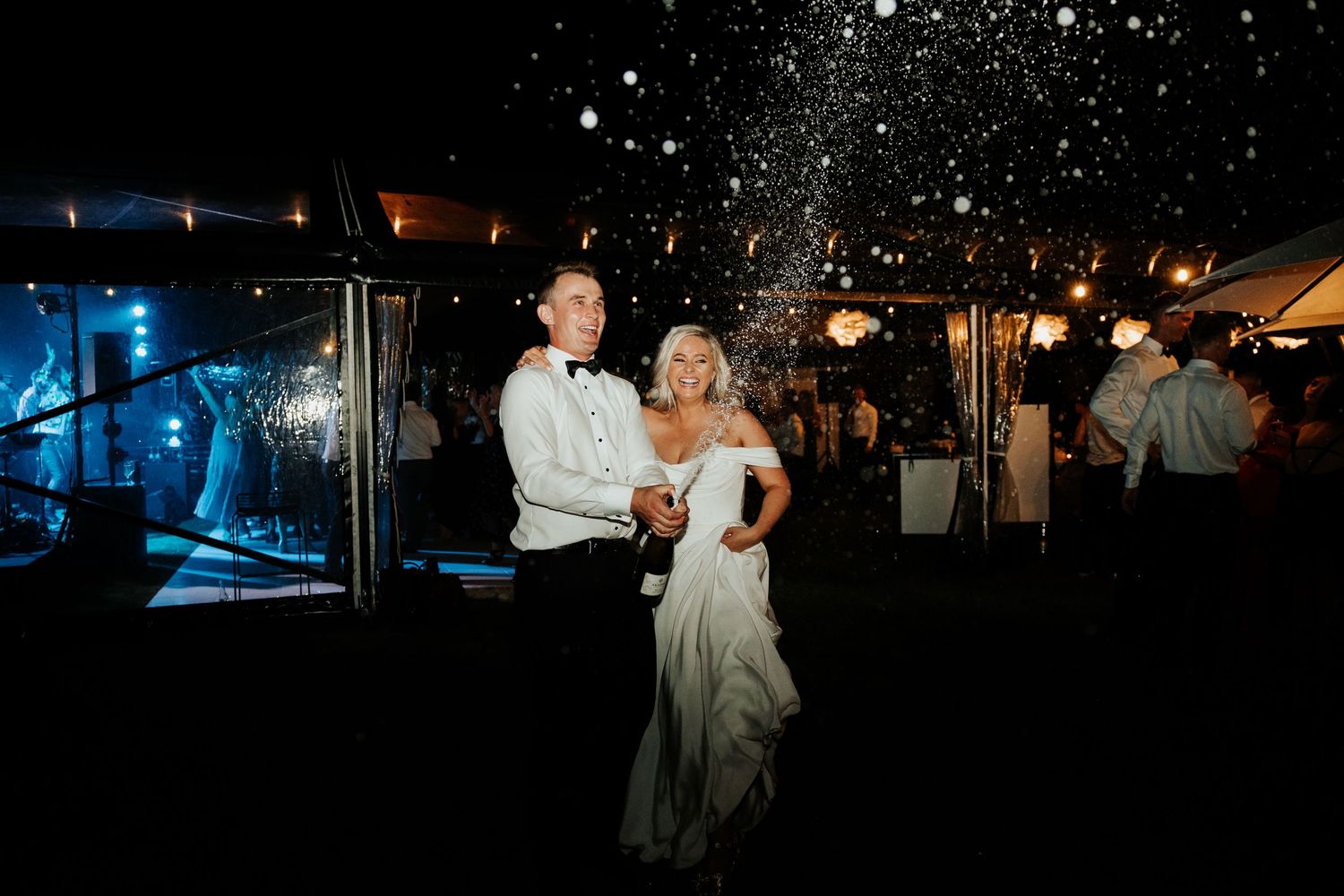 A couple dancing under sparkling lights at an outdoor evening reception.