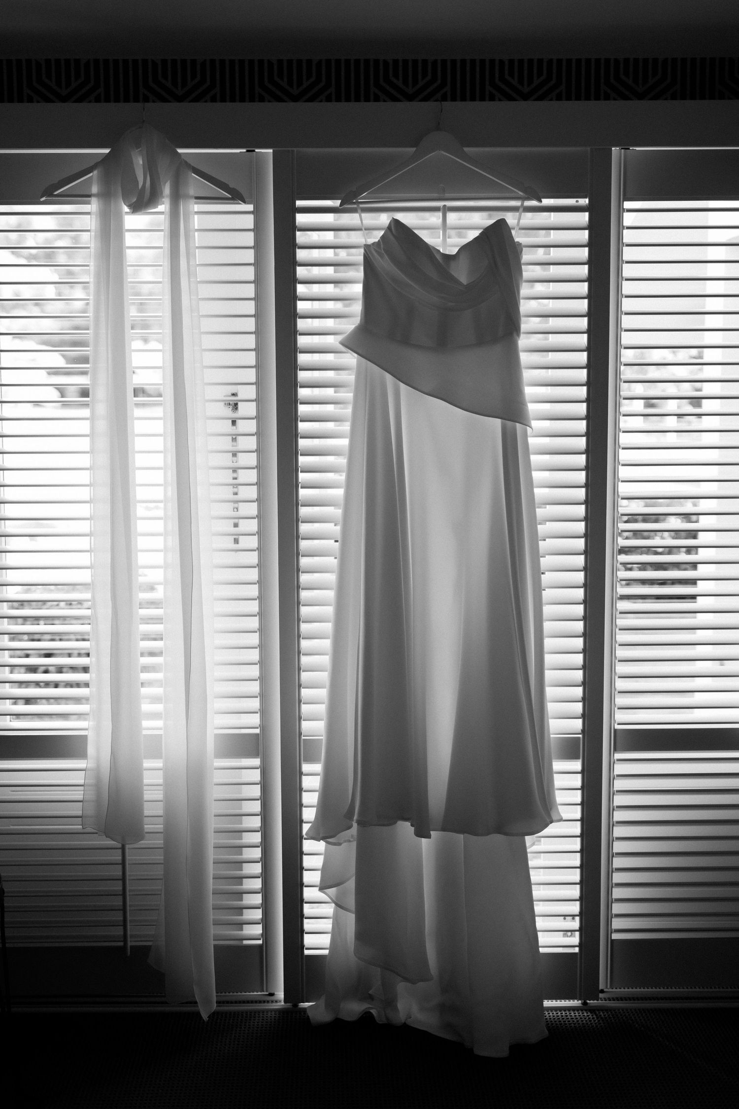 A two-tone wedding dress hanging in front of venetian blinds in black and white.