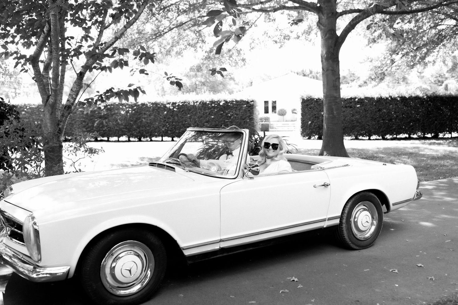 Classic white Mercedes-Benz convertible photographed in black and white against hedges.