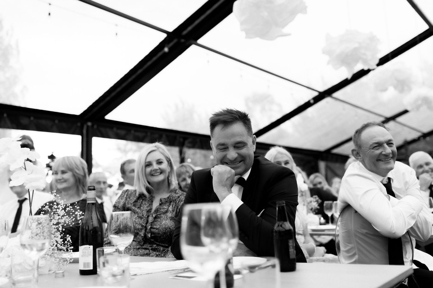 Wedding guests enjoy a candid moment during the reception under a clear tent.